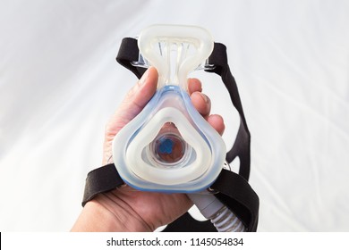 Male hand holding CPAP mask over white bed