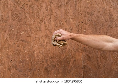 
Male Hand Holding A Crumpled Paper Bag On A Chipboard Background