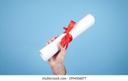 Male Hand Holding Diploma With A Red Ribbon.