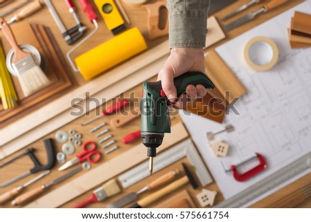 Male hand holding a drill, hardware and work tools on background, top view, do it yourself and home renovation concept