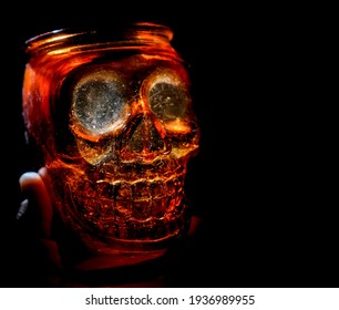 Male Hand Holding Empty Jar In The Form Of Human Skull Isolated On Black Background. 