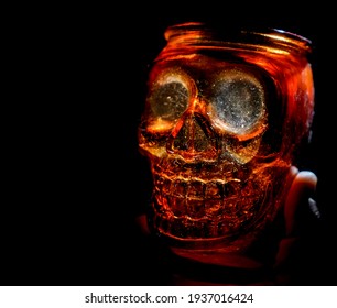 Male Hand Holding Empty Jar In The Form Of Human Skull Isolated On Black Background. 