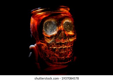 Male Hand Holding Empty Jar In The Form Of Human Skull Isolated On Black Background. 