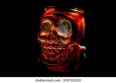 Male Hand Holding Empty Jar In The Form Of Human Skull Isolated On Black Background. 