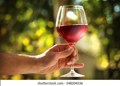 Male Hand Holding Glass With Wine On Blurred Natural Background