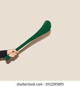 A Male Hand Holding Green Hurling Stick, Hurley Against Beige Background.