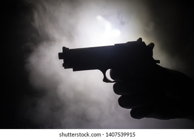 Male Hand Holding Gun On Black Background With Smoke Toned Back Lights. Silhouette Of A Gun In Hand. Crime Concept. Selective Focus