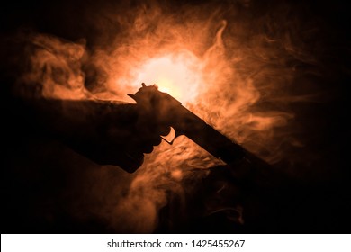 Male Hand Holding Gun On Black Background With Smoke Toned Back Lights. Silhouette Of A Gun In Hand. Crime Concept. Selective Focus