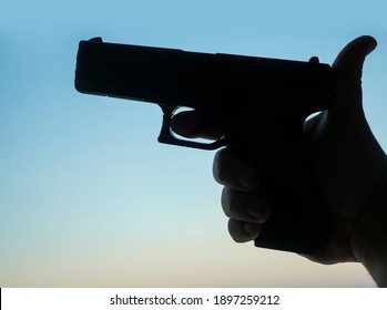 Male Hand Holding Gun On Blue Sky Background. Silhouette Of  Black Pistol. 