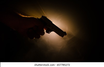 Male hand holding gun on black background with smoke ( yellow orange red white ) colored back lights