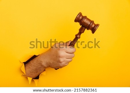 Male hand holding a judge's gavel through torn yellow background. Law and auction aconcept