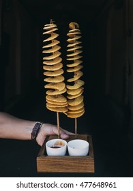 Male hand holding korean tornado potato (Twist Potato) box with sauces on a black background. Traditional street food in South Korea and Taiwan