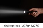 Male hand holding a led flashlight with a wide white beam on a black background, leaving the right side of the frame.