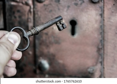 male Hand holding metal vintage historical key to unlocking old iron rusty door, film tone color. Antique door lock and key.