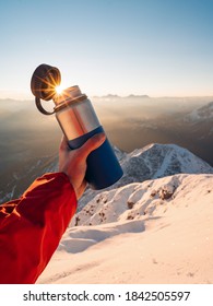 Male Hand Holding Metal Water Bottle. Mountains And Snow During Sunrise In The Background. Reusable Water Bottle. Walking On Winter Day, Holding Travel Stainless Steel Mug With Hot Coffee Or Tea