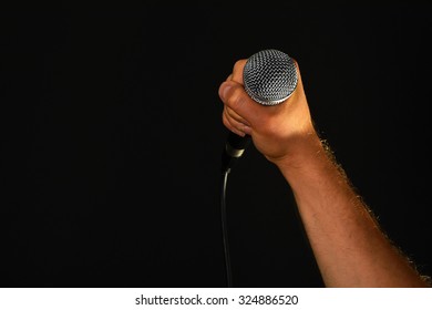 Male Hand Holding Microphone With Wire Cable Isolated On Black Background