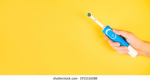 Male hand holding modern electric toothbrush on yellow background. Banner, copy space. Controlled oral hygiene tool, ad space.