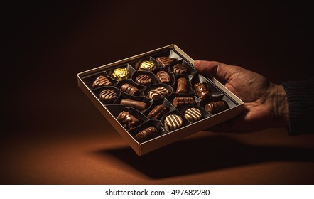 Male Hand Is Holding An Open Box Of Chocolates. 