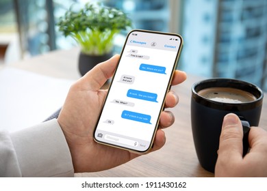 male hand holding phone with app messenger over table in office