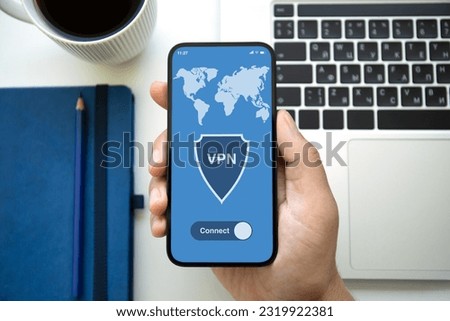 male hand holding phone with app vpn on screen over table with laptop in office