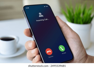 male hand holding phone with incoming call on screen table with coffee in office