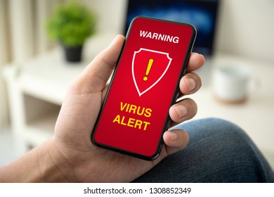 male hand holding phone with warning virus alert alarm on screen in room - Powered by Shutterstock