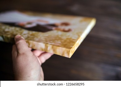 Male hand holding a photography with gallery stretch on a wooden frame. Printed wedding photo on canvas. Lateral side closeup. Selective focus