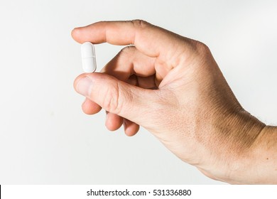 Male Hand Holding A Pill Against White Background