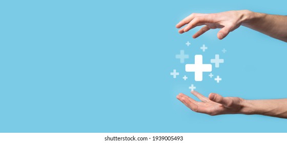 Male hand holding plus icon on blue background. Plus sign virtual means to offer positive thing (like benefits, personal development, social network)Profit,health insurance, growth concepts. - Shutterstock ID 1939005493