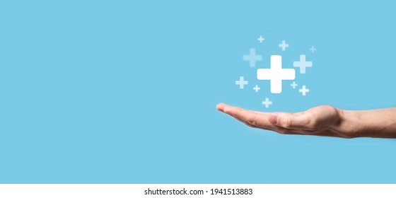 Male hand holding plus icon on blue background. Plus sign virtual means to offer positive thing (like benefits, personal development, social network)Profit,health insurance, growth concepts. - Shutterstock ID 1941513883
