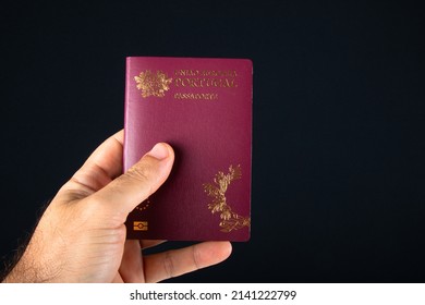 Male hand holding portuguese passport over black background.
