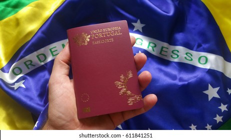 Male hand holding Portuguese passport with Brazilian flag in background