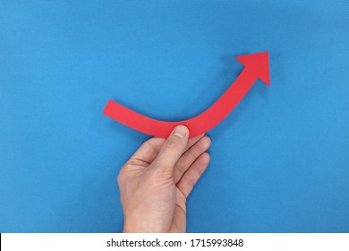 Male Hand Holding A Red Arrow Graph Going Upward In Blue Background. Business Recovery, Growth, Bounce Back Concept.