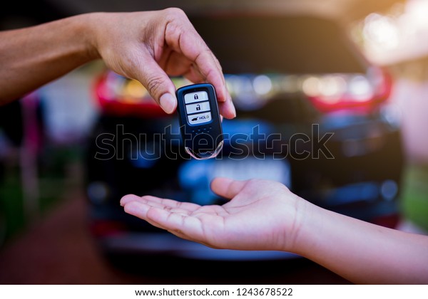 Male hand holding a remote car key and\
handing it over to give another person with blurry car black car in\
garage of house\
background.