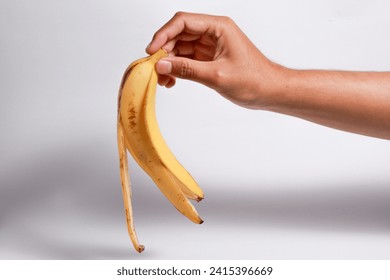 Male hand holding a ripe banana skin on isolated white background. - Powered by Shutterstock - Get 15% off with code: PIKWIZARD15