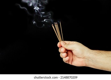 Male hand holding set of smoldering incense sticks with aroma smoke on dark background - Powered by Shutterstock