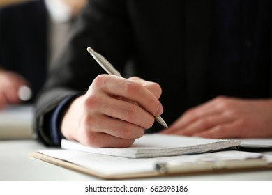 Male hand holding silver pen ready to make note in opened notebook sheet. Businessman in suit at workspace make thoughts records at personal organizer, white collar conference, signature concept