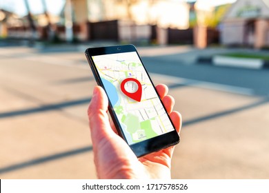 Male hand holding holding smartphone with online-a map on which the geolocation icon. In the background, a blurred street. Close up. Concept of online navigation and GPS