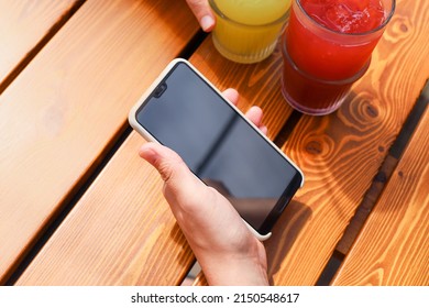 Male hand holding smartphone and two lemonades on brown red glossy boards wooden table. Top view, mockup, close-up. - Powered by Shutterstock