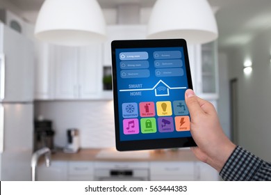 male hand holding tablet with app smart home on background kitchen in house