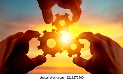 Male Hand Holding Three Wooden Cog Gear Wheel On Blue Sky Background. Sunshine And Yellow Sky .