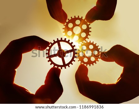 Male hand holding three wooden cog gear wheel on blue sky background. sunshine and yellow sky .