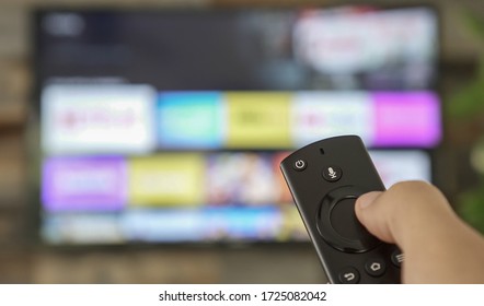 Männliche Hand, die die Fernbedienung des Fernsehers hält und die Fernsehkanäle wechselt. Kanalsurfen, auf die Hand und Fernbedienung fokussiert. Internet TV.