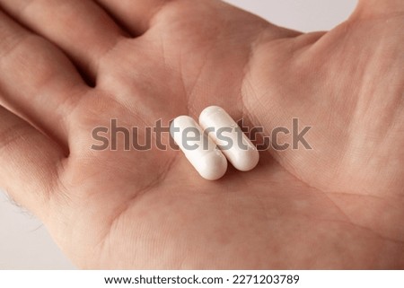 Male hand holding two pills in hand on grey background, taking Your medication. Close up