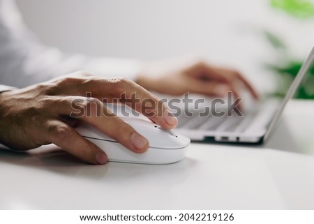 Male hand holding white computer mouse with laptop in office