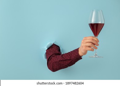 Male Hand Holding Wine Glass And Breaking Through Blue Paper Background.