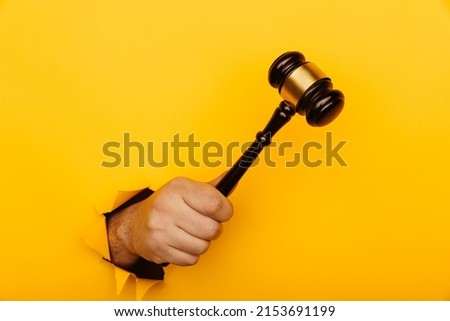 Male hand holding a wooden gavel through torn yellow background. Law and auction aconcept