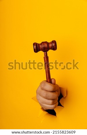 Male hand holding a wooden gavel through torn yellow background. Law and auction aconcept. Vertical image