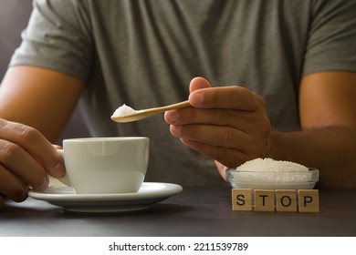 Male hand holding wooden spoon with sugar over cup of coffee or tea. Stop sugar. Campaign against diabetes, obesity, dental caries. Reduce sugar intake. Healthy lifestyle concept.