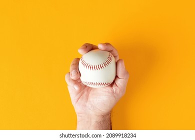 Male hand holds a baseball ball on yellow background. Top view. - Powered by Shutterstock